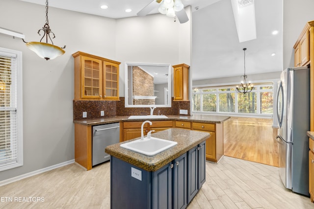 kitchen featuring light wood-type flooring, ceiling fan with notable chandelier, stainless steel appliances, pendant lighting, and a center island with sink