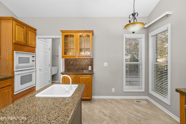 kitchen featuring dark stone counters, white appliances, sink, decorative light fixtures, and light hardwood / wood-style flooring