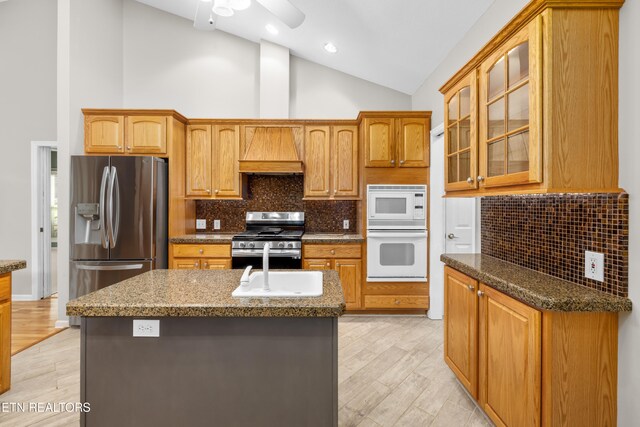 kitchen featuring light hardwood / wood-style flooring, high vaulted ceiling, an island with sink, appliances with stainless steel finishes, and custom exhaust hood