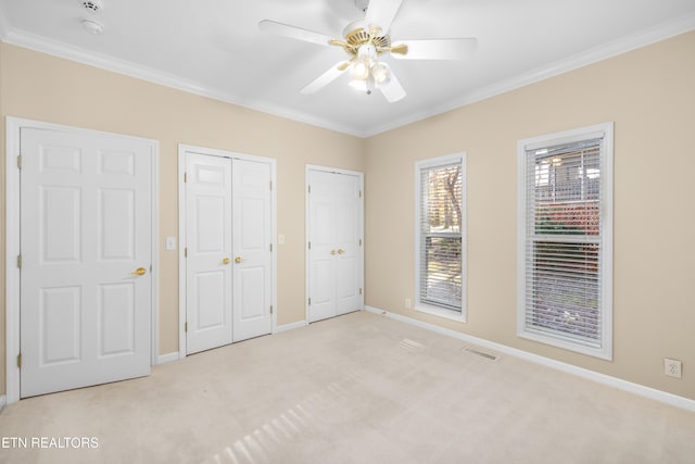 unfurnished bedroom featuring multiple closets, light carpet, ceiling fan, and ornamental molding