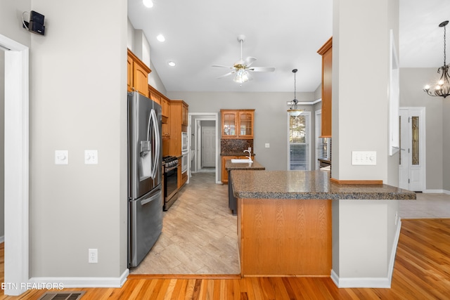 kitchen featuring kitchen peninsula, ceiling fan with notable chandelier, stainless steel appliances, decorative light fixtures, and light hardwood / wood-style flooring