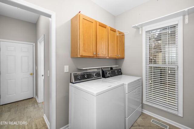 clothes washing area featuring cabinets, washing machine and dryer, and light hardwood / wood-style flooring