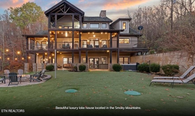 back house at dusk featuring a lawn, a patio area, a balcony, and a fire pit