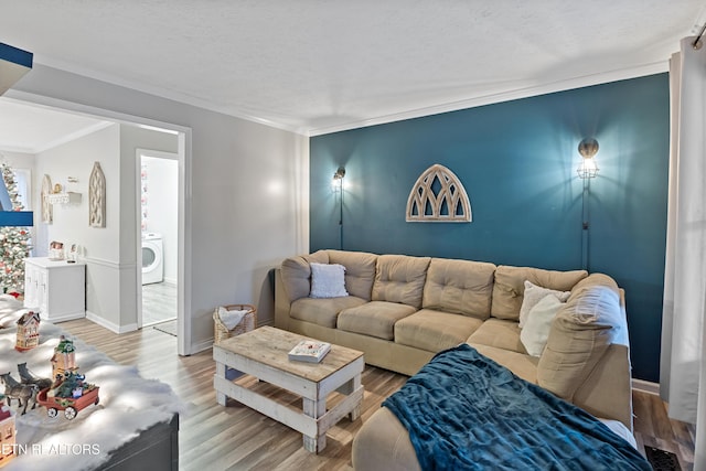 living room featuring baseboards, washer / clothes dryer, wood finished floors, and crown molding