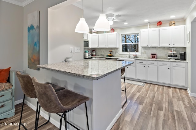 kitchen featuring stainless steel microwave, a breakfast bar area, light wood-style flooring, and crown molding