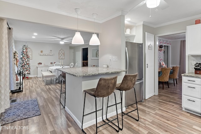 kitchen with ceiling fan, a breakfast bar, freestanding refrigerator, light wood-style floors, and white cabinets