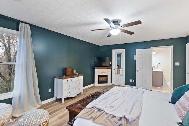 bedroom with a ceiling fan, baseboards, light wood-style flooring, a textured ceiling, and a glass covered fireplace