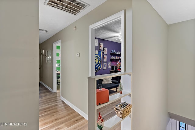 corridor with visible vents, baseboards, a textured ceiling, and light wood-style flooring