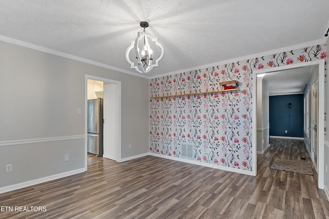 empty room with visible vents, baseboards, an inviting chandelier, wood finished floors, and a textured ceiling