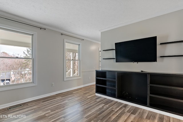 unfurnished living room with visible vents, a healthy amount of sunlight, ornamental molding, wood finished floors, and a textured ceiling