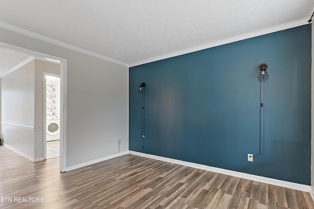 spare room with washer / dryer, wood finished floors, baseboards, and ornamental molding