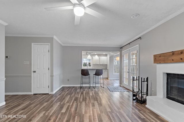 living room featuring a glass covered fireplace, wood finished floors, baseboards, and ornamental molding