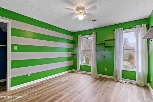 unfurnished room with visible vents, ceiling fan, baseboards, wood finished floors, and a textured ceiling