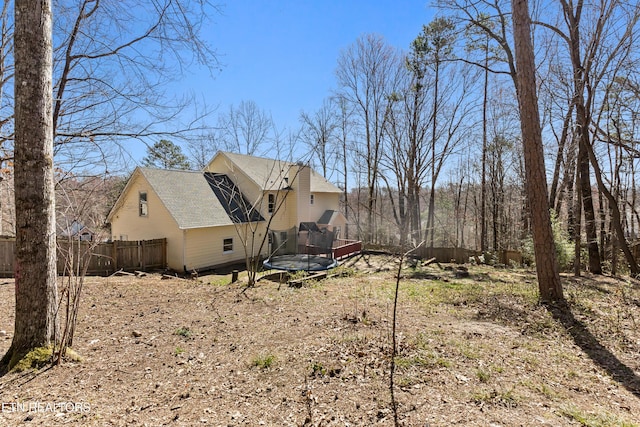 view of property exterior with a trampoline, fence, and roof with shingles