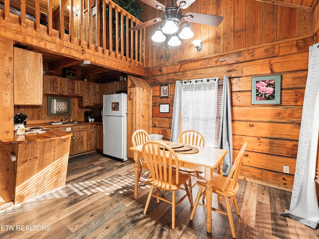 dining area with ceiling fan, sink, a high ceiling, dark hardwood / wood-style flooring, and wood walls