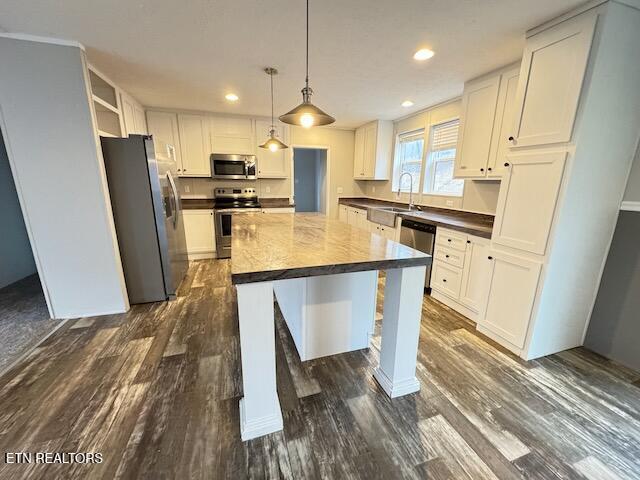 kitchen featuring hanging light fixtures, a kitchen island, dark hardwood / wood-style flooring, white cabinetry, and stainless steel appliances