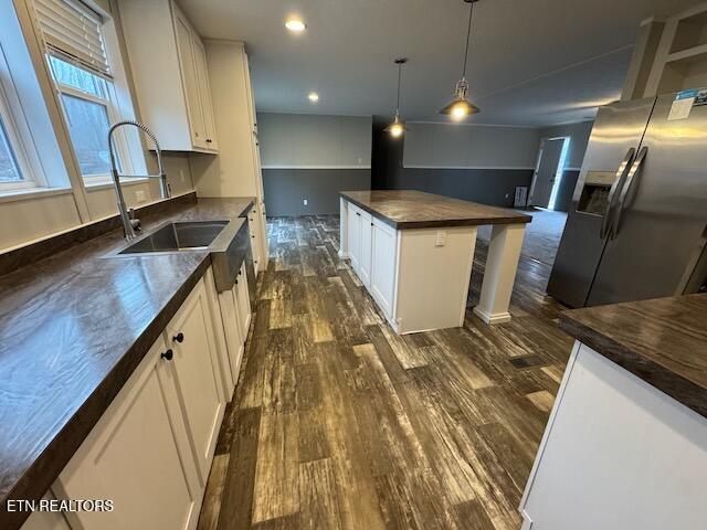 kitchen with white cabinetry, dark hardwood / wood-style flooring, stainless steel refrigerator with ice dispenser, pendant lighting, and a kitchen island