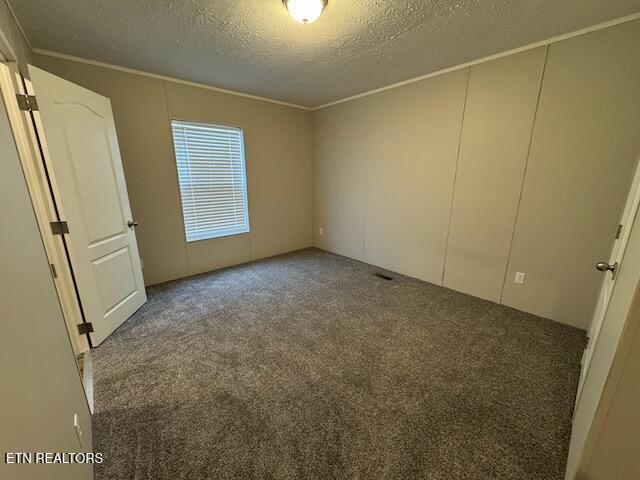 unfurnished bedroom featuring dark colored carpet, ornamental molding, and a textured ceiling