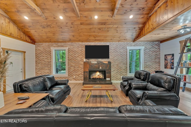 living room featuring lofted ceiling with beams, light hardwood / wood-style flooring, a healthy amount of sunlight, and brick wall