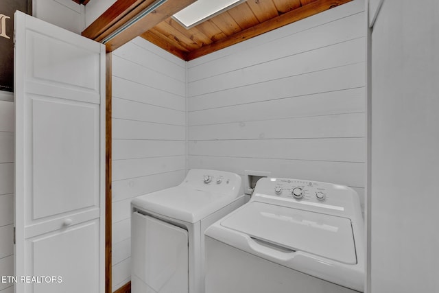 laundry area featuring a skylight, wooden ceiling, wooden walls, and washing machine and clothes dryer