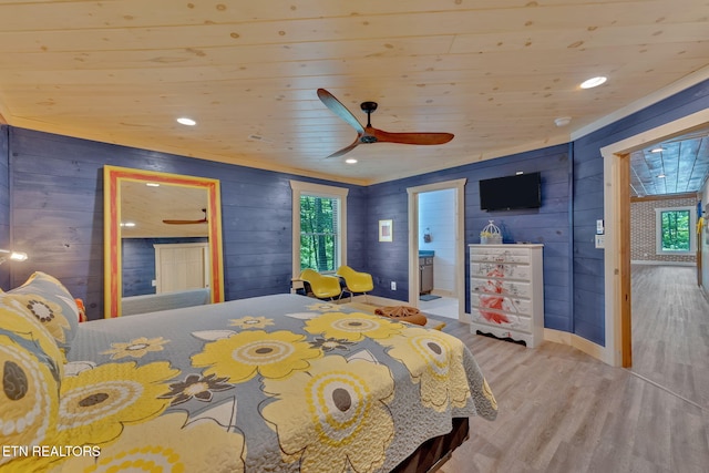 bedroom featuring multiple windows, wood walls, ensuite bathroom, and light hardwood / wood-style floors