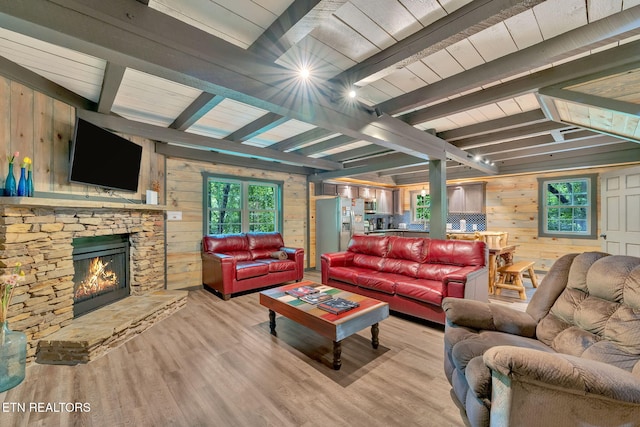 living room with beamed ceiling, light hardwood / wood-style floors, a stone fireplace, and wooden walls