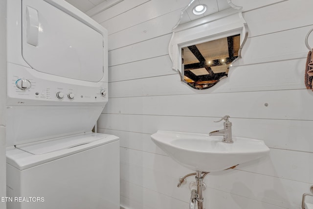 bathroom with sink, wooden walls, and stacked washer and clothes dryer