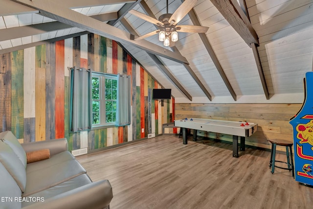 recreation room with vaulted ceiling with beams, ceiling fan, wood walls, and light hardwood / wood-style floors