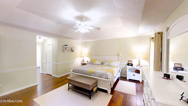 bedroom featuring dark wood-type flooring, ceiling fan, a textured ceiling, a tray ceiling, and a closet