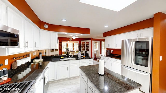 kitchen featuring appliances with stainless steel finishes, dark stone counters, ceiling fan, sink, and white cabinetry