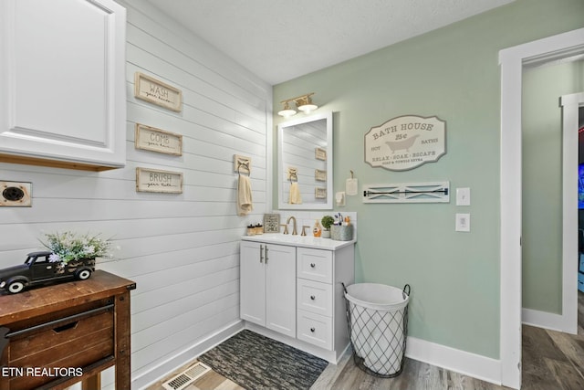 bathroom with wooden walls, vanity, a textured ceiling, and hardwood / wood-style flooring