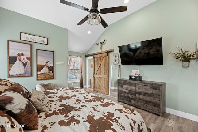 bedroom with a barn door, ceiling fan, light hardwood / wood-style flooring, and vaulted ceiling