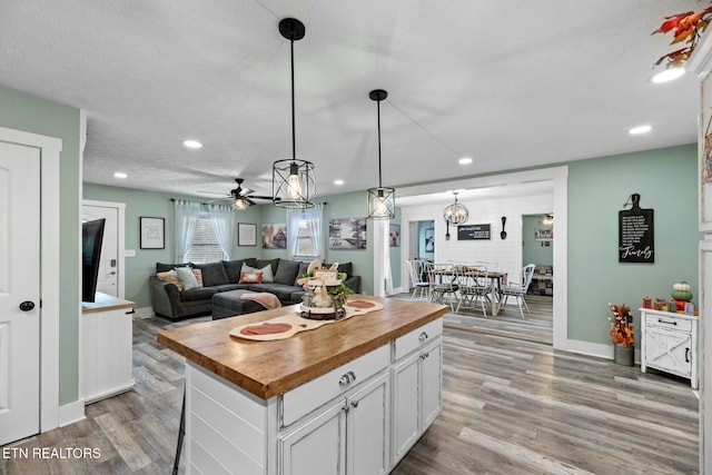 kitchen featuring wood counters, light wood-type flooring, decorative light fixtures, white cabinets, and a kitchen island