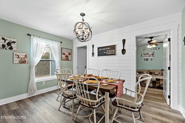 dining space featuring hardwood / wood-style floors, ceiling fan with notable chandelier, and wood walls