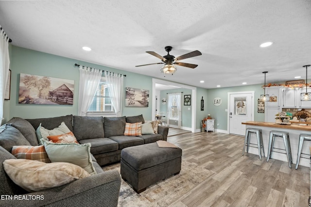 living room with ceiling fan, light hardwood / wood-style flooring, and a textured ceiling