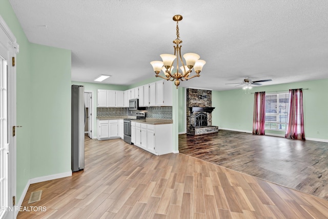 kitchen featuring a brick fireplace, a textured ceiling, stainless steel appliances, white cabinets, and light hardwood / wood-style floors