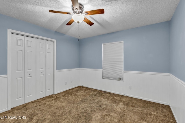 unfurnished bedroom featuring dark colored carpet, a textured ceiling, a closet, and ceiling fan