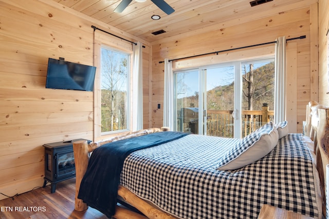 bedroom featuring access to exterior, wood-type flooring, wooden walls, and multiple windows