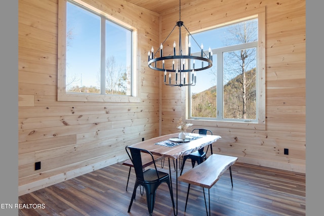 dining space with wood walls, dark wood-type flooring, and a notable chandelier