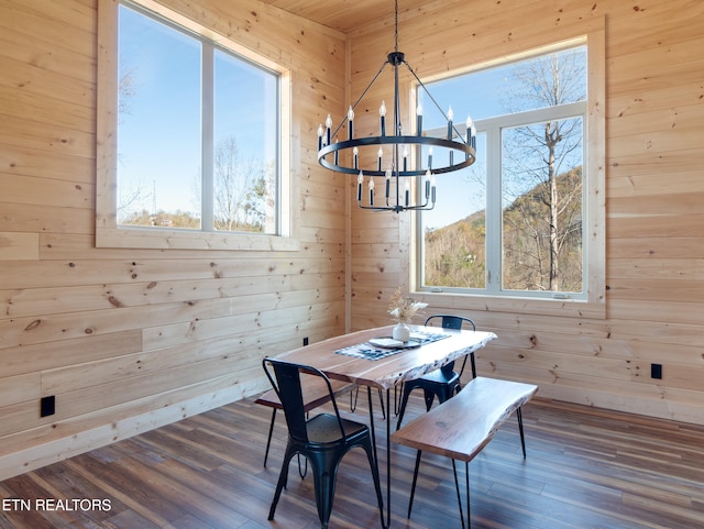 dining space with wooden walls, dark wood-type flooring, and an inviting chandelier