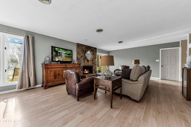 living room with light hardwood / wood-style floors, a stone fireplace, and a wealth of natural light