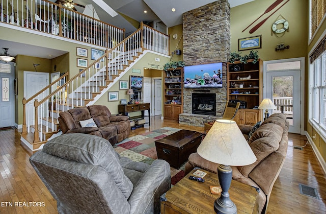 living room with ceiling fan, light hardwood / wood-style floors, a fireplace, and a high ceiling