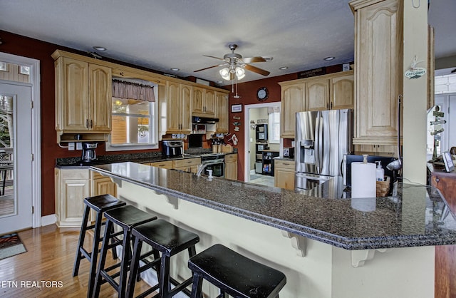 kitchen with kitchen peninsula, light wood-type flooring, ceiling fan, stainless steel fridge with ice dispenser, and a breakfast bar area