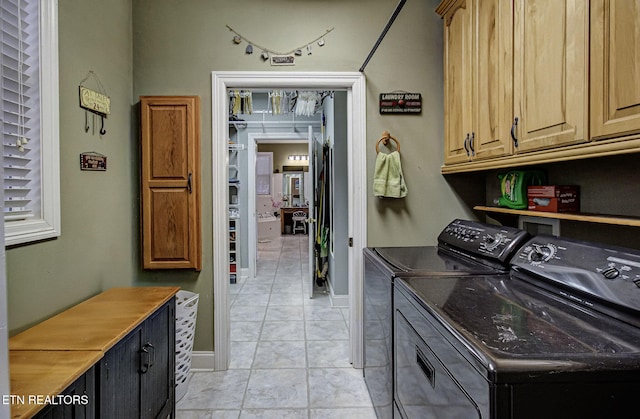 clothes washing area with cabinets, light tile patterned floors, and washing machine and clothes dryer