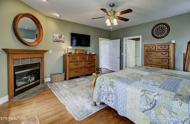 bedroom with a tiled fireplace, ceiling fan, and hardwood / wood-style flooring