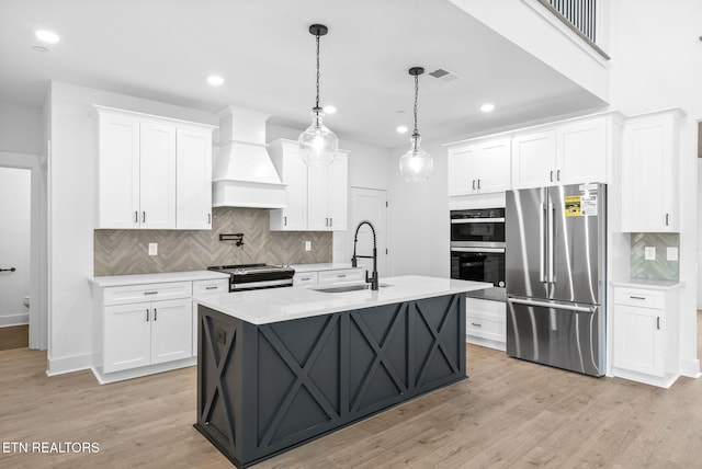 kitchen with custom range hood, stainless steel appliances, sink, white cabinets, and light hardwood / wood-style floors