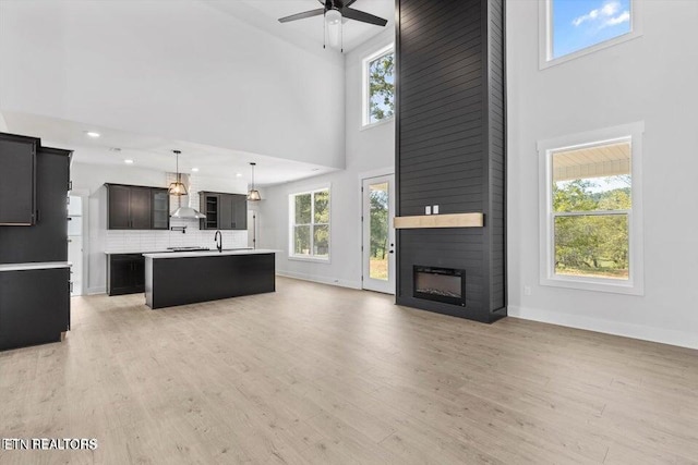 unfurnished living room with ceiling fan, a fireplace, a high ceiling, and light hardwood / wood-style flooring