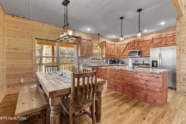 kitchen with a center island, wood walls, pendant lighting, light hardwood / wood-style floors, and appliances with stainless steel finishes