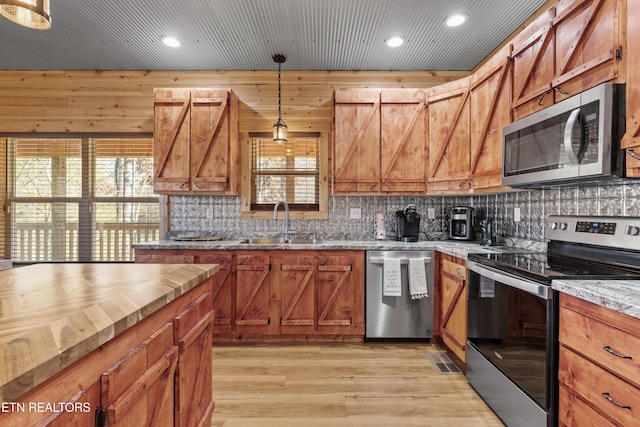 kitchen with appliances with stainless steel finishes, sink, pendant lighting, light hardwood / wood-style floors, and wood walls