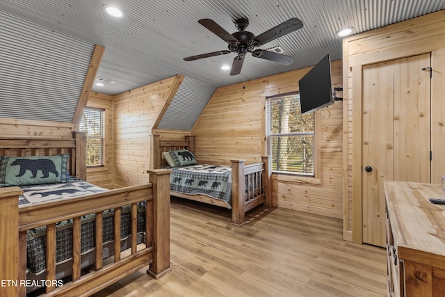 bedroom with ceiling fan, vaulted ceiling, wooden walls, and light hardwood / wood-style flooring